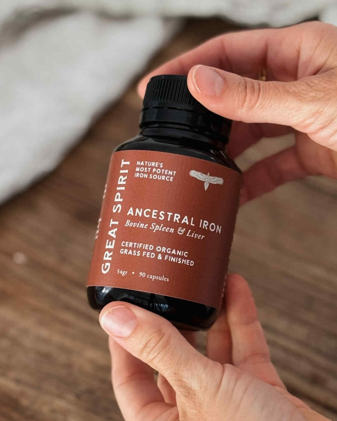 Hand holding a bottle of Great Spirit Ancestral Iron supplement on a wooden surface.